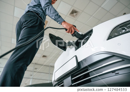 Plugging the charger. Handsome car dealership worker is with electric vehicle 127484533
