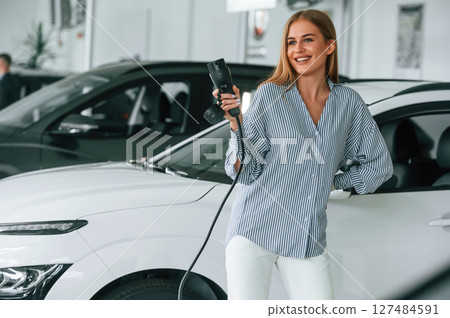 Holding charger for electric car. Beautiful woman is indoors 127484591