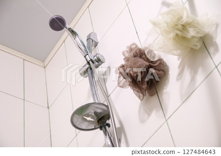 A silver shower head and a white washcloth on clean tiles in a modern bathroom, ready for a refreshing shower. Spotless white tiles frame a silver shower head and a fresh washcloth A silver shower head and a white washcloth on clean tiles in a modern bathroom, ready for a refreshing shower. Spotless white tiles frame a silver shower head and a fresh washcloth 127484643