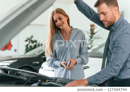 Man in formal clothes is with woman customer with the electric car 127484744