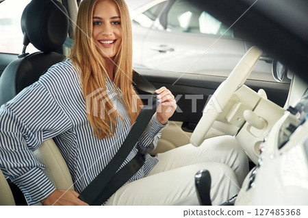 Wearing seating belt. Beautiful woman is indoors with the modern car Wearing seating belt. Beautiful woman is indoors with the modern car 127485368