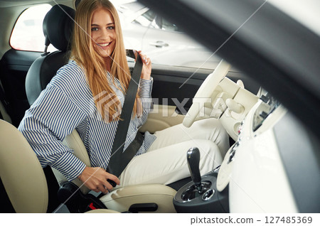 Wearing seating belt. Beautiful woman is indoors with the modern car 127485369