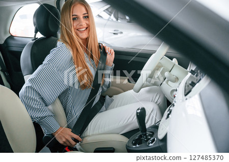Wearing seating belt. Beautiful woman is indoors with the modern car Wearing seating belt. Beautiful woman is indoors with the modern car 127485370