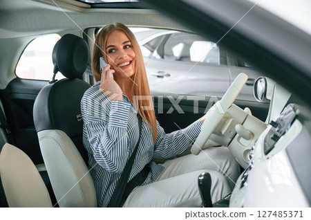 Sitting inside aand talking by phone. Beautiful woman is indoors with the modern car 127485371