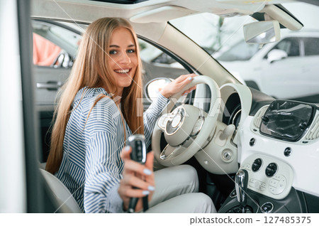 Showing the keys of new automobile. Beautiful woman is indoors with the modern car 127485375