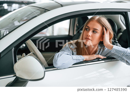 Leaning on the door with opened window. Beautiful woman is indoors with the modern car Leaning on the door with opened window. Beautiful woman is indoors with the modern car 127485390