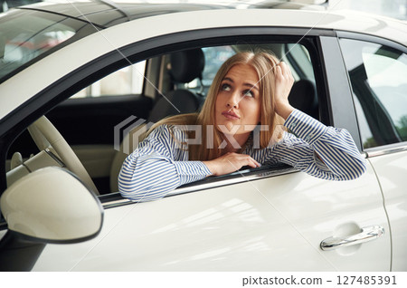Leaning on the door with opened window. Beautiful woman is indoors with the modern car Leaning on the door with opened window. Beautiful woman is indoors with the modern car 127485391