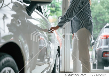 Opening the door. Close up view of woman that is with electric car 127485403