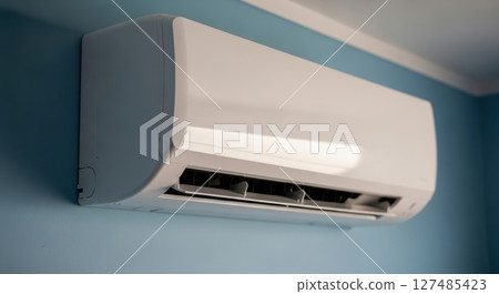 White air conditioner unit mounted on a light blue wall for indoor climate control. 127485423