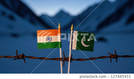 Miniature flags of india and pakistan on barbed wire with mountains, symbolizing border conflict 127485431