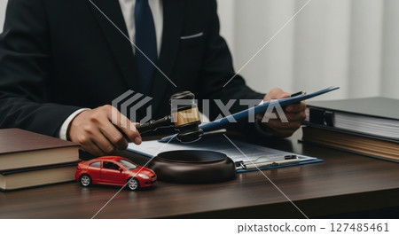 Lawyer holding a gavel with legal documents and a miniature car on a desk 127485461