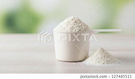 White protein powder in a measuring scoop with a small pile on a light surface 127485511