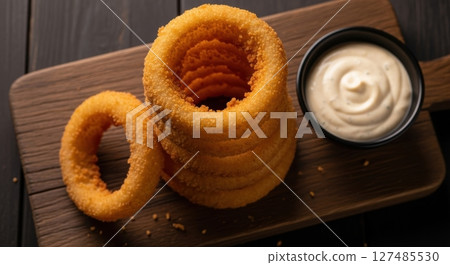 Golden crispy onion rings with dipping sauce on a rustic wooden board Golden crispy onion rings with dipping sauce on a rustic wooden board 127485530