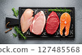 Fresh raw assortment of chicken, pork, beef, and salmon on a dark cutting board 127485568