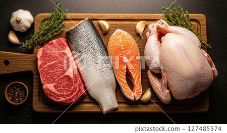 Raw beef steak, whole fish, salmon, and chicken on a wooden board with herbs and spices. 127485574