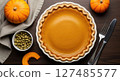 Delicious pumpkin pie in a white fluted dish with pumpkins and cutlery on a wooden table. 127485577