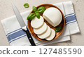 Fresh mozzarella cheese, whole and sliced, with basil leaves and a kitchen knife 127485590