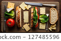 Assorted cheese, fresh bread, and vegetables on a rustic wooden board with a sandwich. 127485596