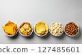 Assortment of popular snacks including chips, crackers, popcorn, and pretzels in bowls on a grey surface 127485601