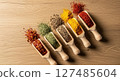 Five colorful spices in wooden scoops arranged diagonally on a light wooden surface. 127485604