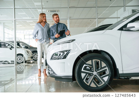 Choosing the automobile. Man in formal clothes is with woman customer with the electric car 127485643