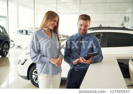 Information in the notepad. Man in formal clothes is with woman customer with the electric car Information in the notepad. Man in formal clothes is with woman customer with the electric car 127485647