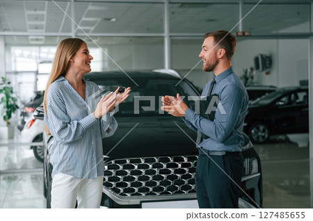 Buying the automobile, taking keys. Man in formal clothes is with woman customer with the electric car 127485655