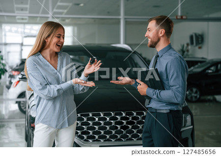 Buying the automobile, taking keys. Man in formal clothes is with woman customer with the electric car Buying the automobile, taking keys. Man in formal clothes is with woman customer with the electric car 127485656