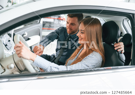 Explaining how automobile works. Man in formal clothes is with woman customer with the electric car Explaining how automobile works. Man in formal clothes is with woman customer with the electric car 127485664