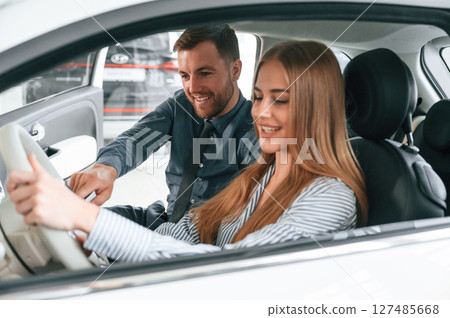 Showing the controls of the automobile, sitting. Man in formal clothes is with woman customer with the electric car 127485668