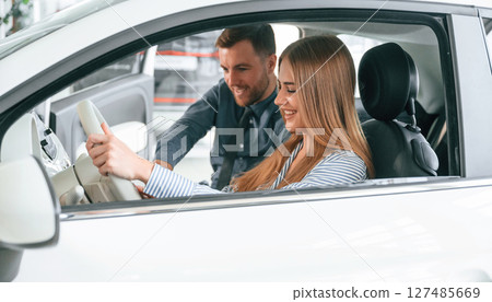 Showing the controls of the automobile, sitting. Man in formal clothes is with woman customer with the electric car 127485669