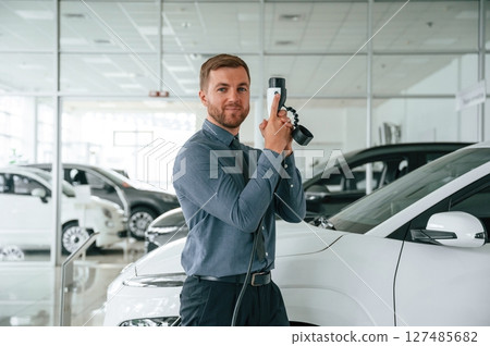 Having fun with charger. Handsome car dealership worker is with electric vehicle Having fun with charger. Handsome car dealership worker is with electric vehicle 127485682