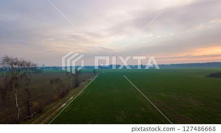 Aerial view on a dramatic and colorful sunrise or sunset sky over a grassy green farmfield shot from 127486668