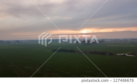 Aerial view on a dramatic and colorful sunrise or sunset sky over a grassy green farmfield shot from 127486678
