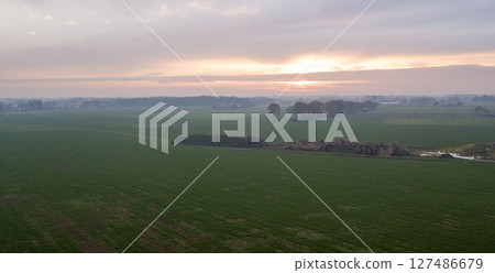 Aerial view on a dramatic and colorful sunrise or sunset sky over a grassy green farmfield shot from 127486679