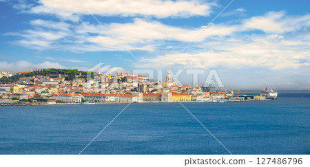 Wide panoramic shot of Lisbon, its beautiful city center, historic buildings, iconic landmarks and Tagus River under blue sky with some white clouds on sunny day. Colorful skyline with castle on hill 127486796