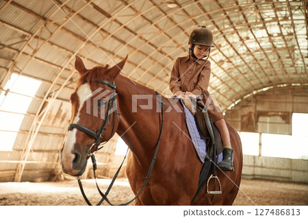 Riding the animal. Cute little girl is with horse indoors Riding the animal. Cute little girl is with horse indoors 127486813