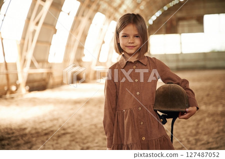 Little girl in jockey clothes is standing indoors Little girl in jockey clothes is standing indoors 127487052