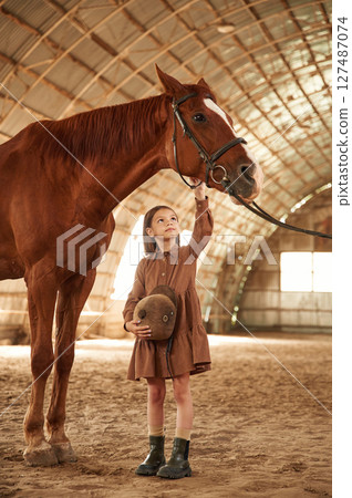 Standing with the animal. Cute little girl is with horse indoors 127487074