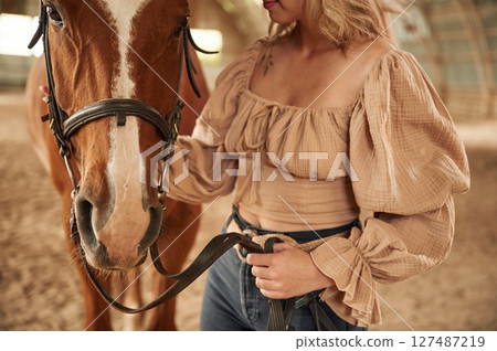 Beautiful young woman is with horse indoors Beautiful young woman is with horse indoors 127487219