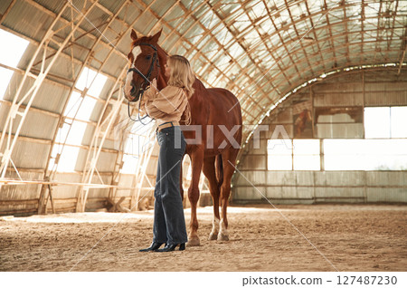 Full height photo. Beautiful young woman is with horse indoors 127487230