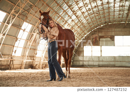 Full height photo. Beautiful young woman is with horse indoors 127487232