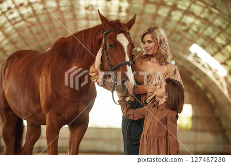 Woman with her little daughter is with horse indoors 127487280