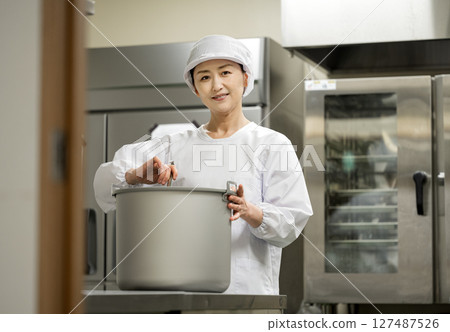 A female chef working in the kitchen of a school lunch center A female chef working in the kitchen of a school lunch center 127487526