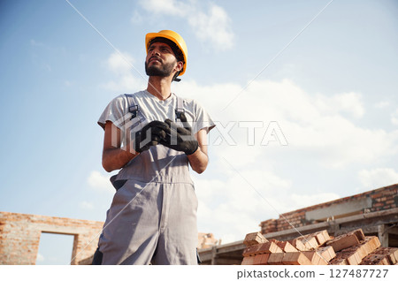 In grey uniform. Handsome Indian man is on the construction site In grey uniform. Handsome Indian man is on the construction site 127487727