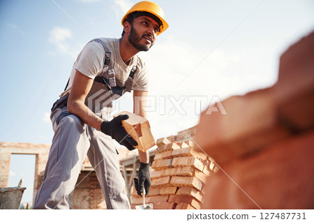 View from below. Brick in hand. Handsome Indian man is on the construction site 127487731