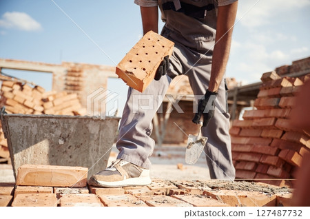In gloves, holding brick. Close up view of man that is working on the construction site 127487732
