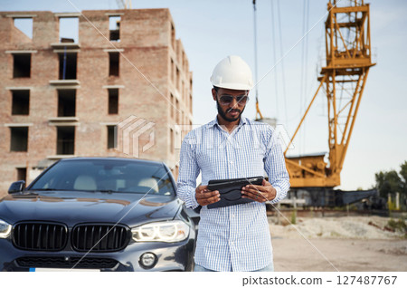Wireless device in hands, digital tablet. Handsome Indian man is on the construction site Wireless device in hands, digital tablet. Handsome Indian man is on the construction site 127487767