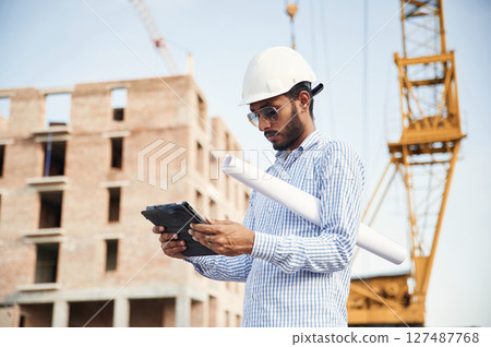 Wireless device in hands, digital tablet. Handsome Indian man is on the construction site Wireless device in hands, digital tablet. Handsome Indian man is on the construction site 127487768
