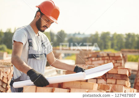 Reading the plan that is in the hands. Handsome Indian man is on the construction site Reading the plan that is in the hands. Handsome Indian man is on the construction site 127487807